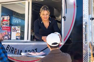 A woman serves food from a food truck to a customer, creating a lively atmosphere and showcasing delicious offerings.