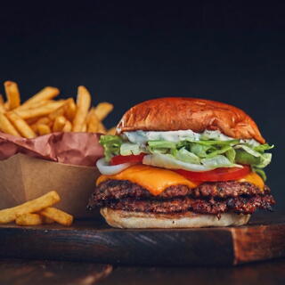 A juicy burger with cheddar, lettuce, tomato, and onion sits next to a serving of crispy French fries, all against a dark background.