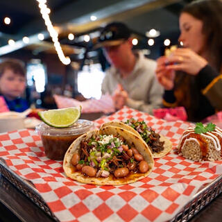 A vibrant spread of tacos with beans, topped with onions and cilantro, served alongside lime and salsa in a lively dining setting.