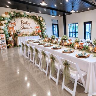 A beautifully decorated baby shower venue features a long dining table with nature-themed decor, greenery, and adorable animal accents.